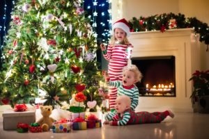 Little children in front of a christmas tree in matching pajamas.