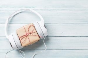 Christmas music gift concept. Headphones and gift box on wooden table. Listen to Christmas music each morning.